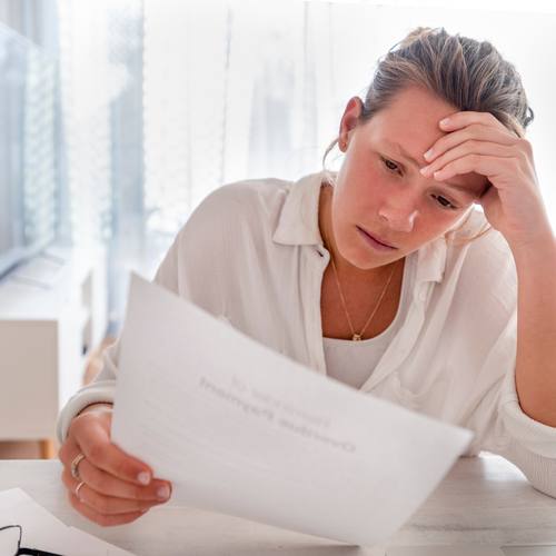 A woman sitting at a table, reading an overdue payment notice with a worried expression